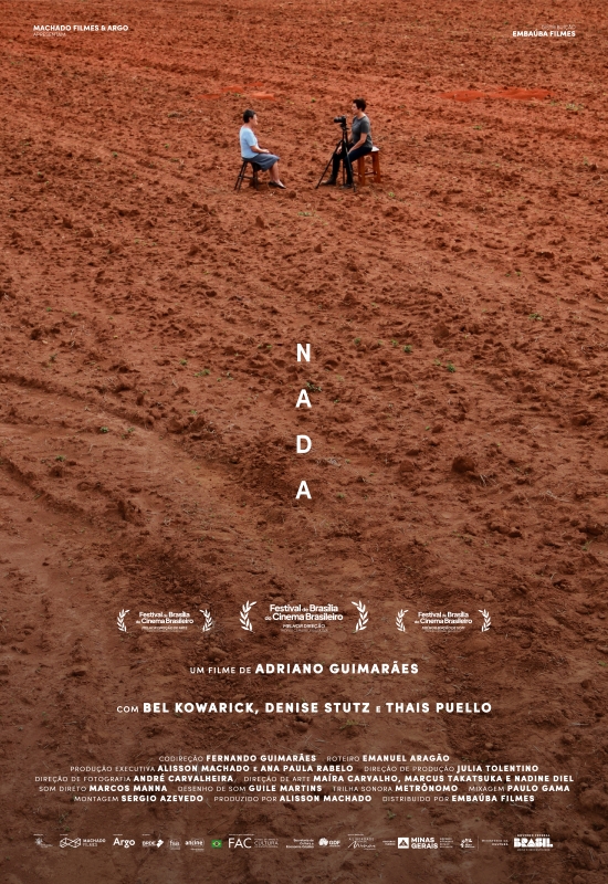 Cartaz de divulgação do filme. A imagem mostra um grande terreno de terra batida, avermelhada e seca, que ocupa quase toda a cena. Na parte superior, ao centro, duas pessoas brancas estão sentadas em cadeiras de madeira, frente a frente. À frente da pessoa da direita, que está com camiseta cinza e calça preta, há uma câmera de vídeo montada em tripé, voltada para a pessoa à esquerda, que veste camiseta azul clara e saia azul. No centro do cartaz, em branco e na vertical, o título: “Nada”. Na parte inferior, em letras menores: “Um filme de Adriano Guimarães. Com Bel Kowarick, Denise Stutz e Thais Puello”.
