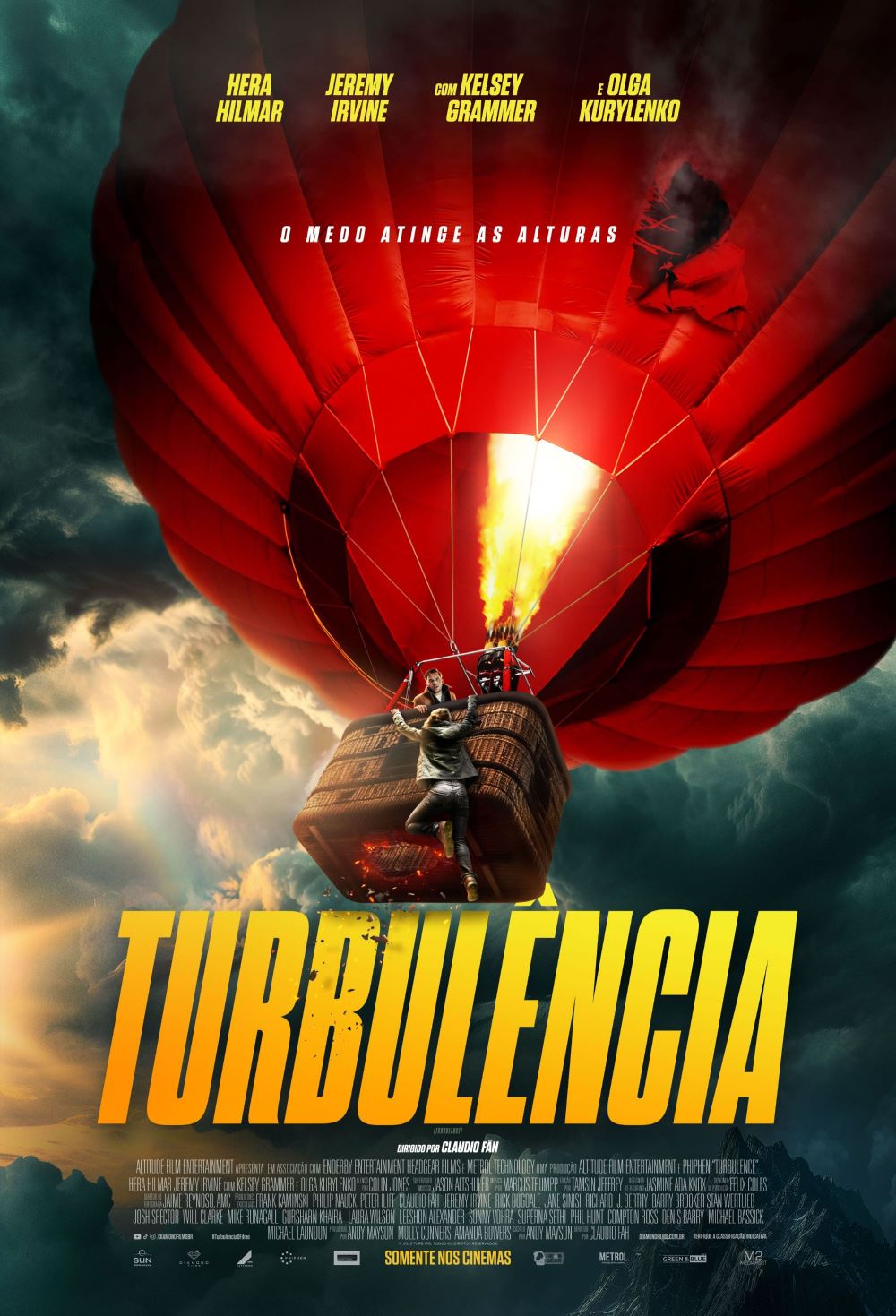 Cartaz de divulgação do filme. Ao fundo, céu com nuvens espessas e escuras. No centro do cartaz, um grande balão vermelho inflado, com gomos visíveis que formam padrões radiais. Mais à direita do tecido inflado, há um rasgo saindo fumaça. Na parte inferior, uma chama intensa saindo do queimador, iluminando a região central. Abaixo do balão está a cesta marrom, com textura trançada. Dentro, uma mulher branca segura a estrutura da borda com uma das mãos e esticando o outro braço para baixo. Fora da cesta, um homem branco está pendurado, com as duas mãos na borda e as pernas suspensas. Na base da cesta, um buraco chamuscado. Na parte superior do cartaz, escrito em letras brancas: “O medo atinge as alturas”. Na região inferior, em letras grandes e amarelas, o título: “Turbulência”.